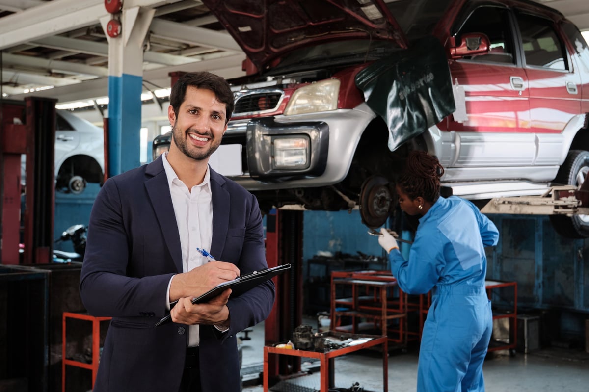 Automotive repair shop manager holding a checklist, smiling, in a service garage